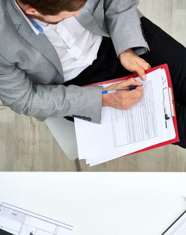 Concentrated bearded manager in formalwear sitting with legs on desk and filling in form, directly above view