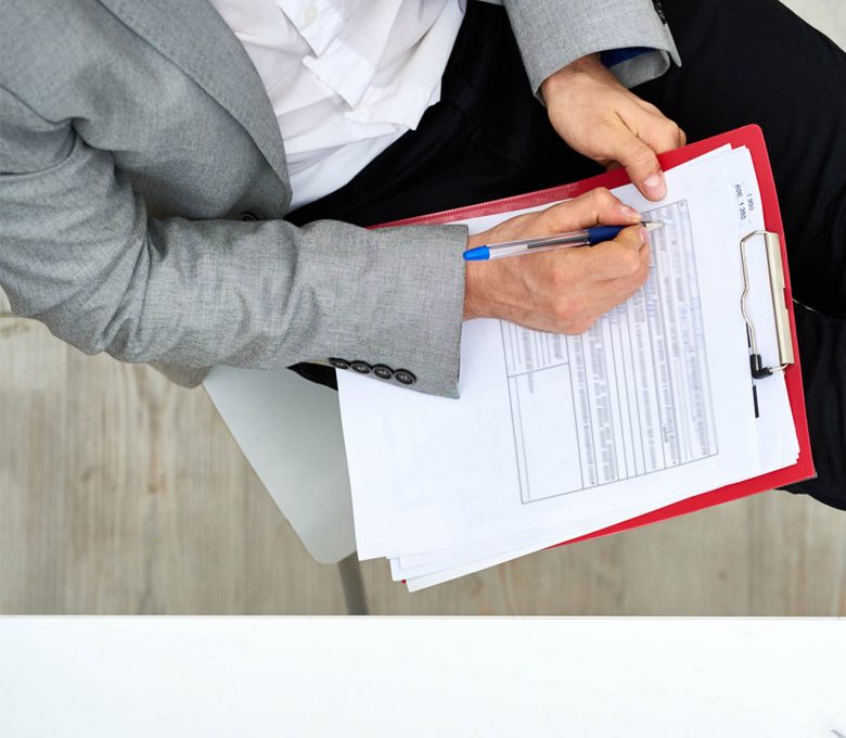 Concentrated bearded manager in formalwear sitting with legs on desk and filling in form, directly above view